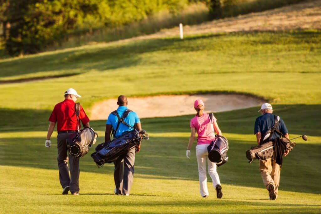 Four golfers walking away on a golf course with their bags over their shoulders on a sunny day.