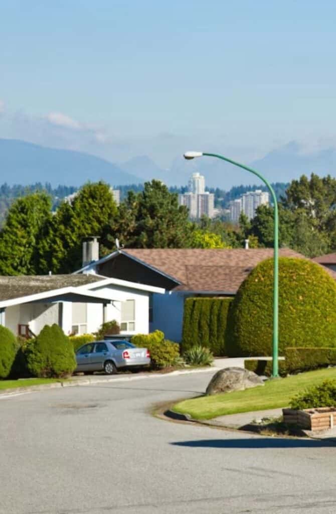 Residential street in North Burnaby showing a house against the backdrop of city towers, mountain range and blue sky in Burnaby, B.C., Canada