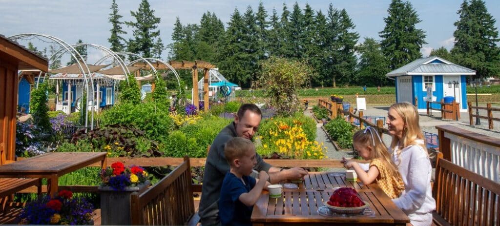 A mom, dad, and school aged son and daughter sitting outside at a wooden table eating ice cream and a strawberry pie on a sunny day at Krauss Berry Farm in Langley, B.C. Canada.