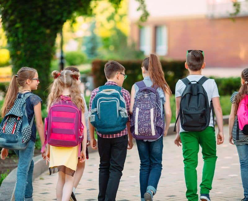 A group of middle school aged children walking to school with their colourful backpacks on their back on a sunny day.