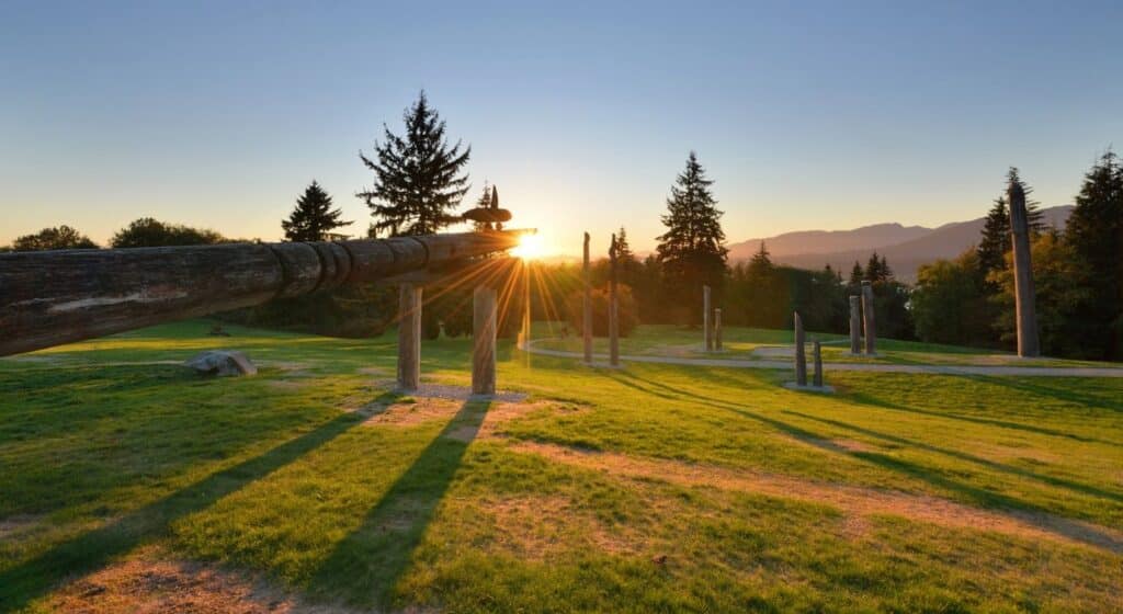 Kushiro Park totems and conservation area and tall trees in Burnaby Mountain against blue sky and sunset.