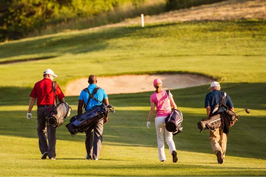 Four golfers walking away on a golf course with their bags over their shoulders on a sunny day.